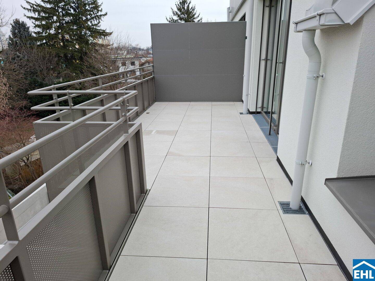 Lange, geflieste Terrasse mit modernem Metallgeländer und Blick auf die Umgebung.