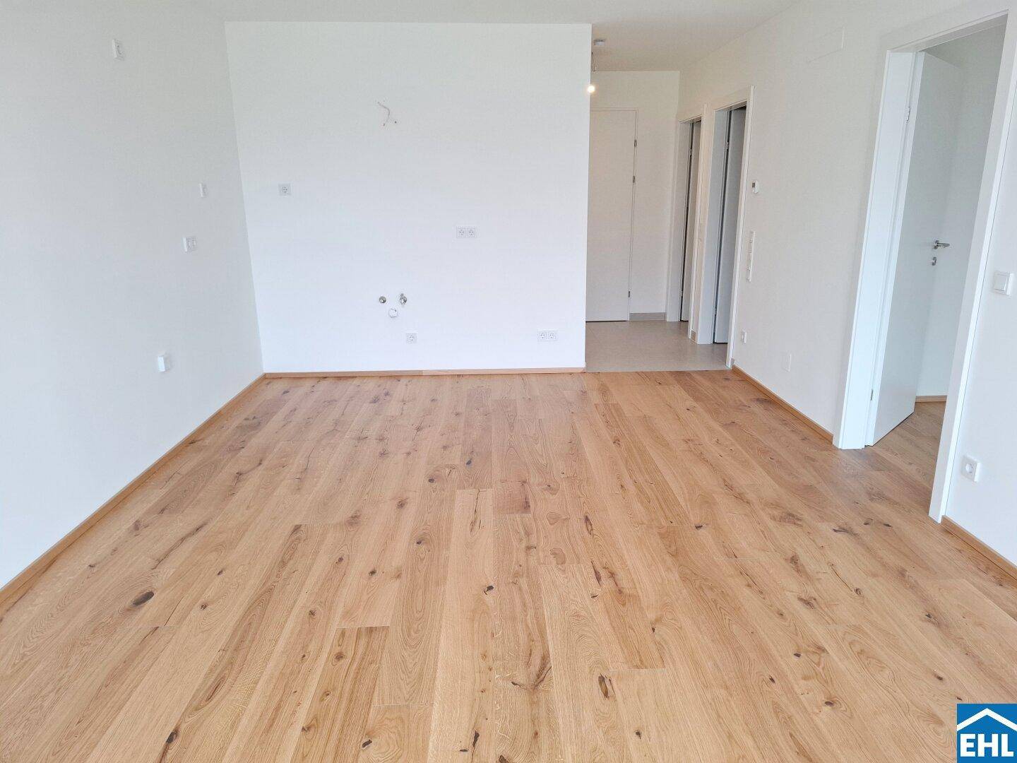 Geräumiger, heller Wohnbereich mit hochwertigem Parkettboden und weiß gestrichenen Wänden.