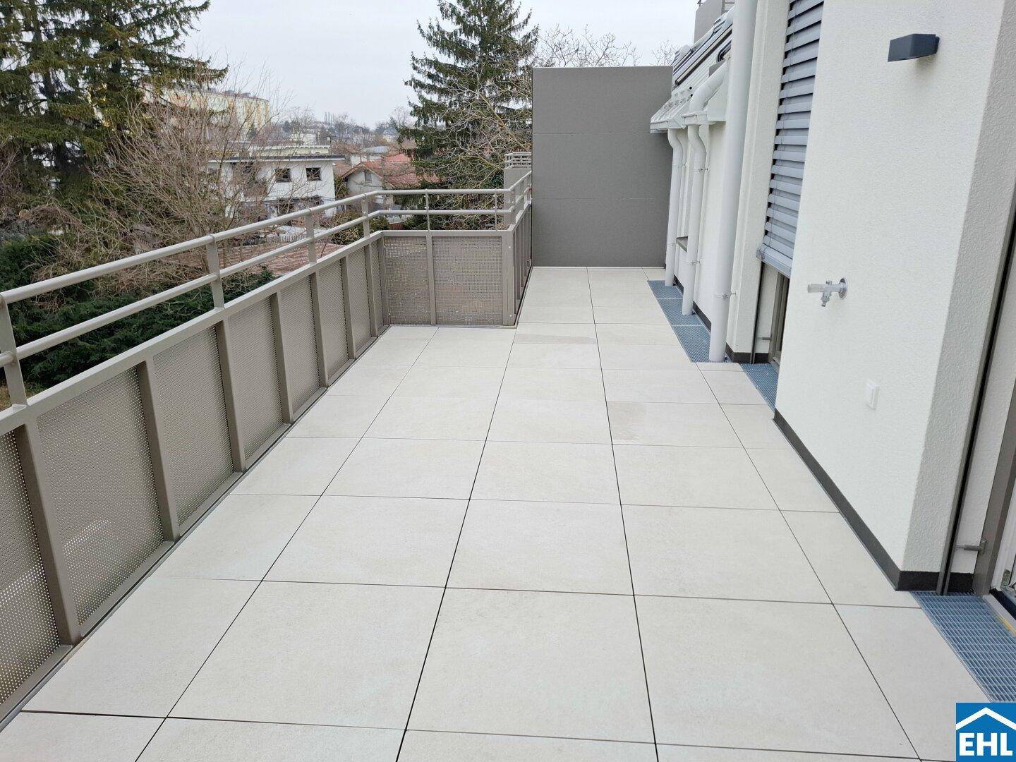 Breiter Balkon mit hellen Fliesen und modernem Metallgeländer, ideal für Entspannung im Freien.