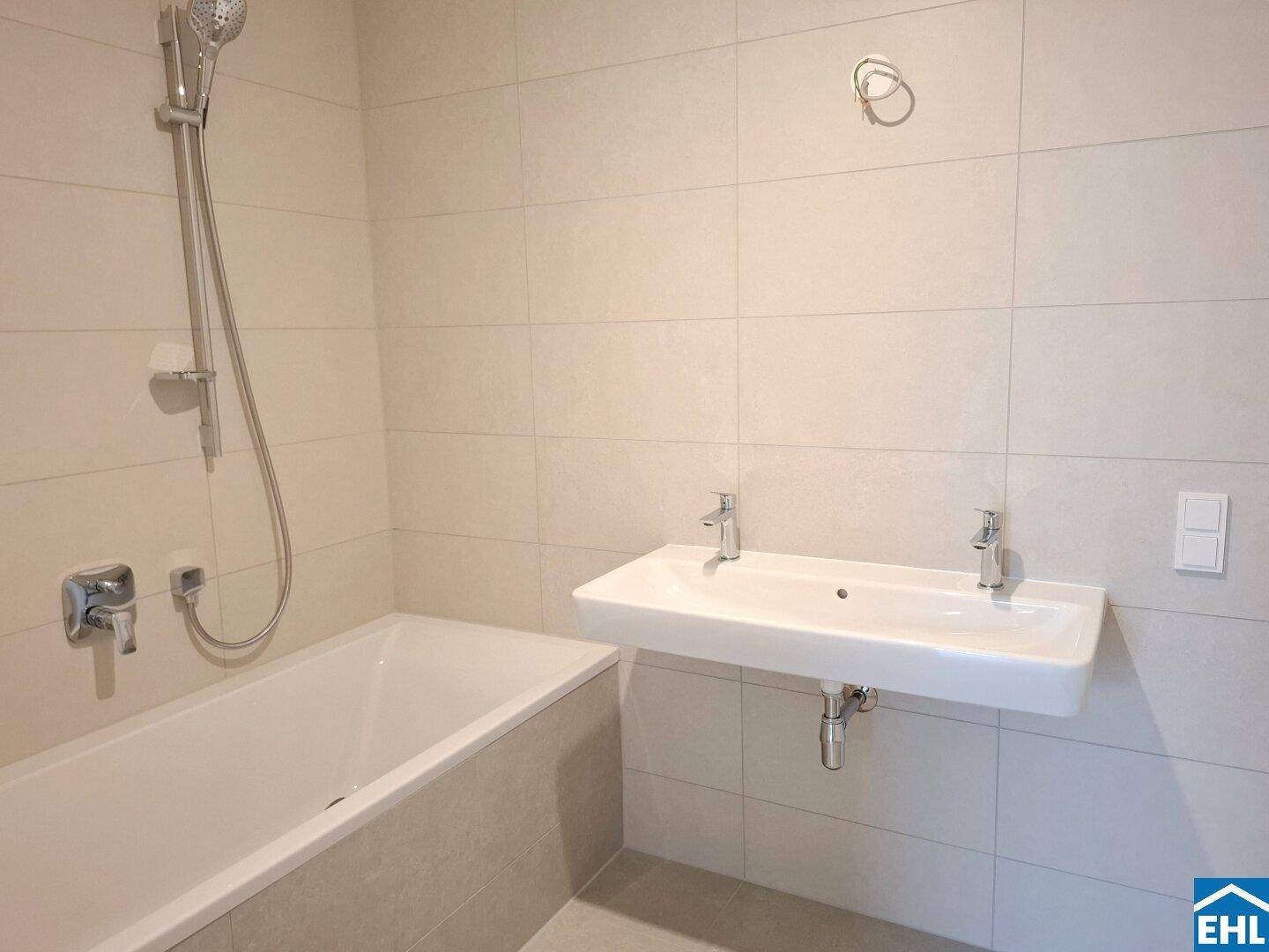 Modernes Badezimmer mit Badewanne, Doppelwaschbecken und hellen Fliesen, in neuwertigem Zustand.