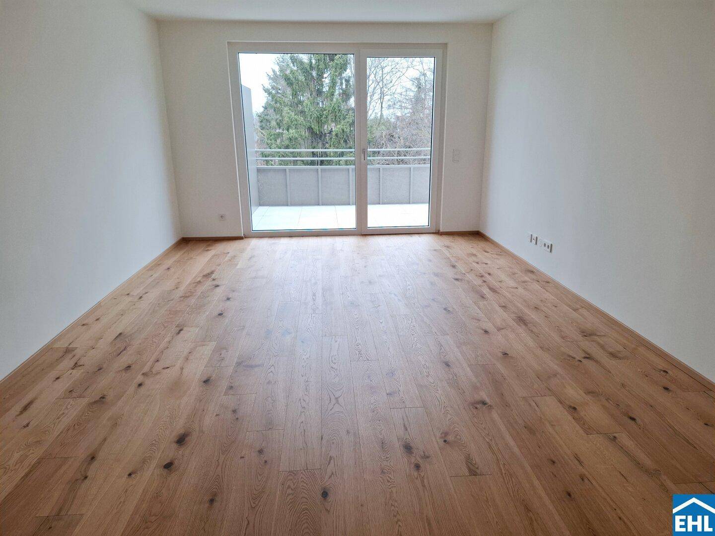 Geräumiges, helles Zimmer mit Holzboden und großen Fenstern zum Balkon, unmöbliert.