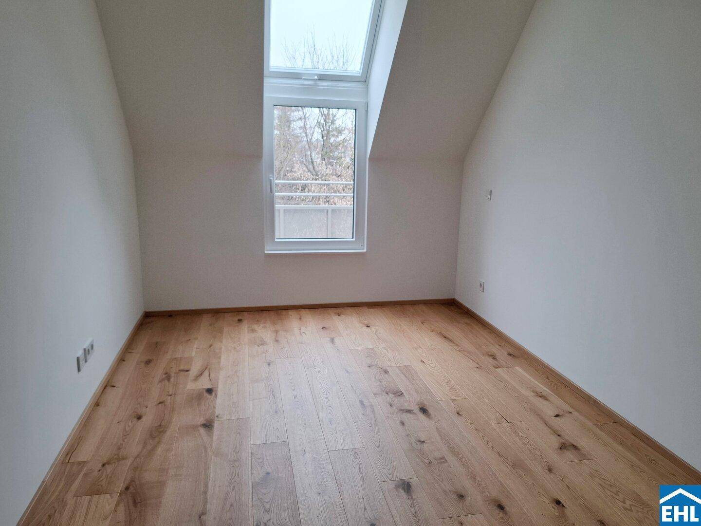 Dachgeschosszimmer mit Holzboden, Dachfenster und schrägen Wänden, ideal als Schlafzimmer.