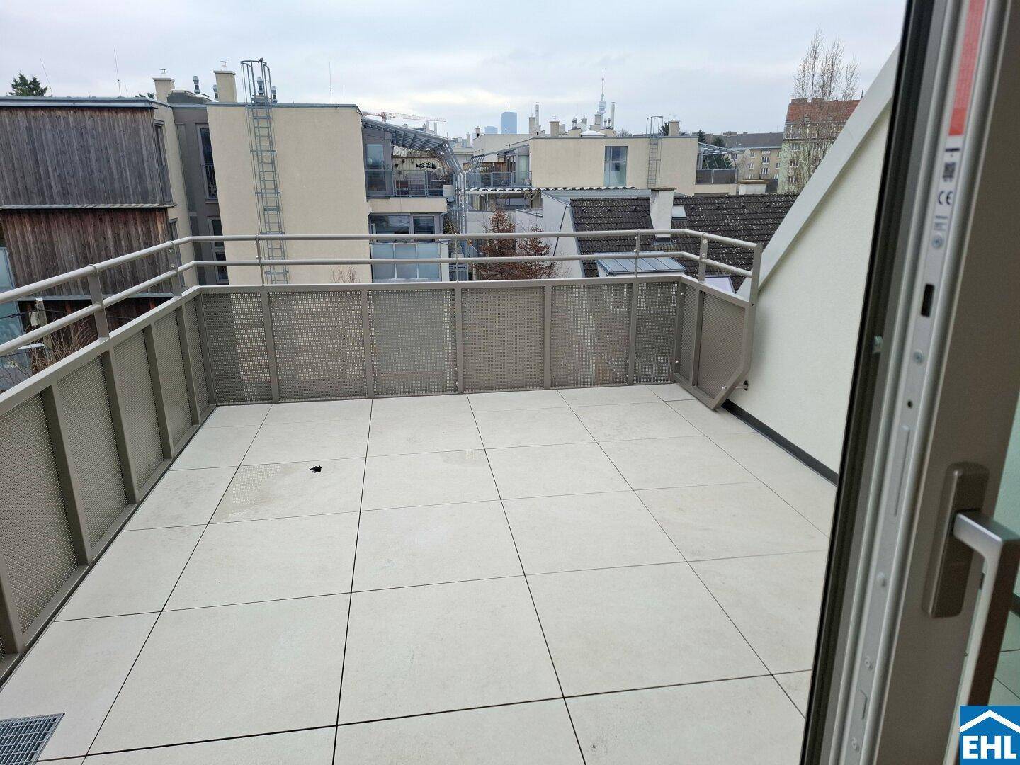 Großer Balkon mit Fliesenboden und Blick auf die umliegenden Gebäude und den Horizont.