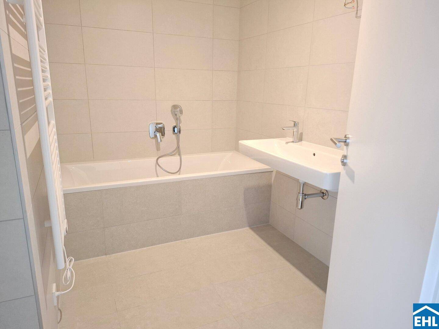 Helles Badezimmer mit Badewanne, modernem Waschbecken und großformatigen Fliesen an Wänden und Boden.