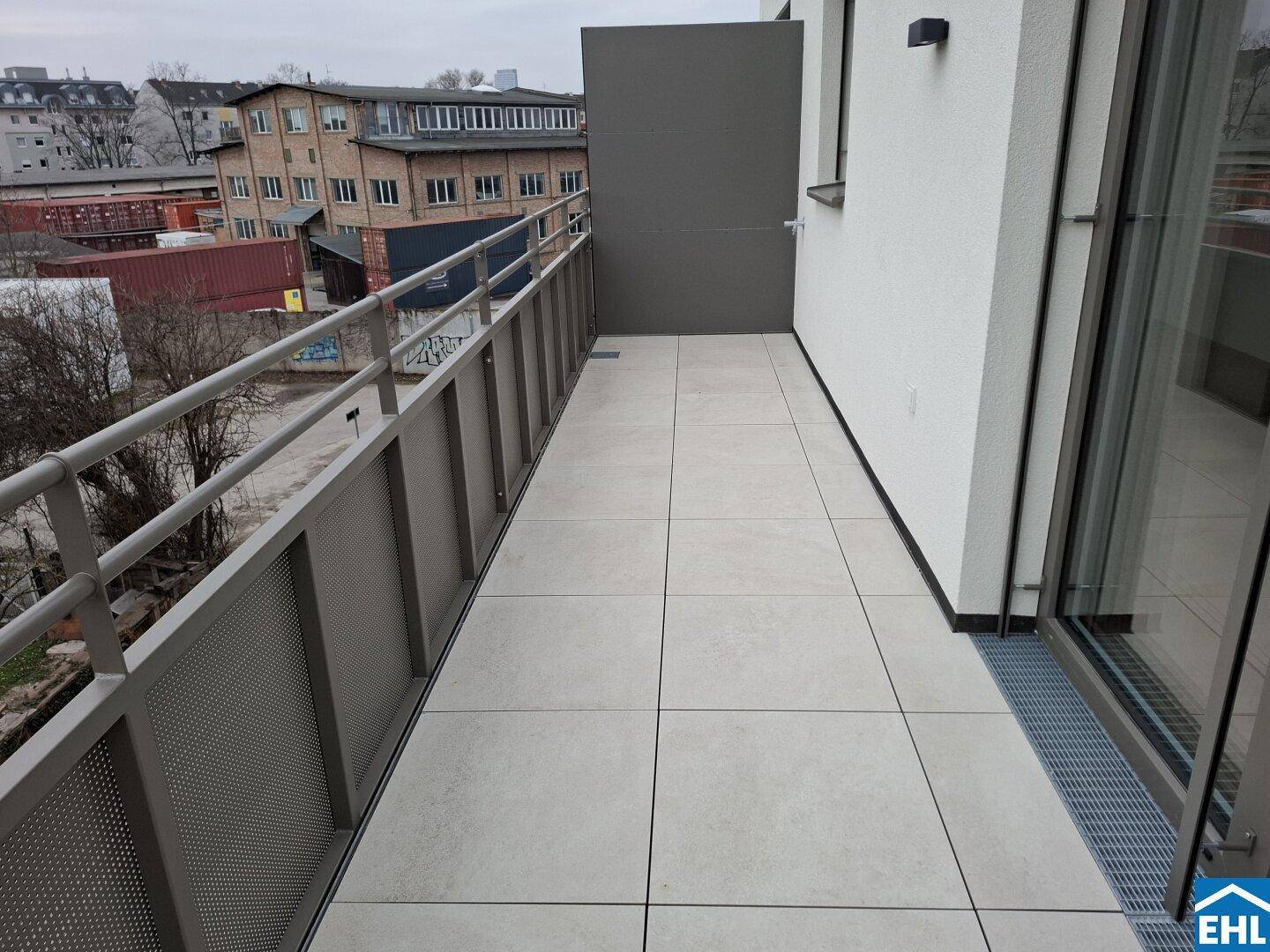 Langer Balkon mit hellen Fliesen und Metallgeländer, bietet einen Blick auf die Umgebung.