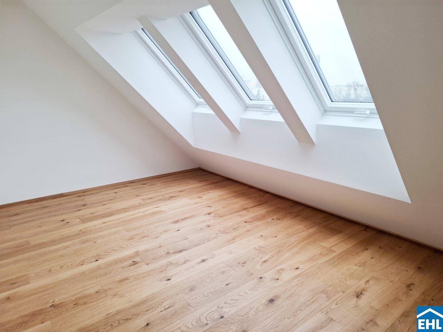 Dachgeschosszimmer mit schrägen Wänden, hellem Parkettboden und mehreren Dachfenstern für viel Licht.