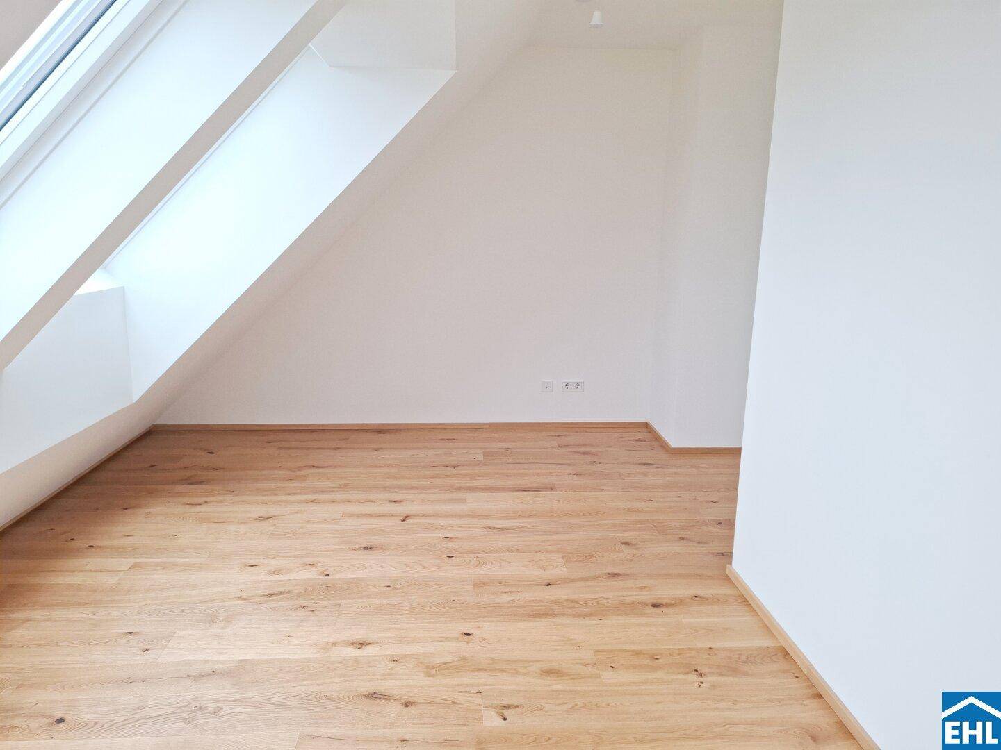 Helles Dachzimmer mit Holzboden und schrägen Wänden, ausgestattet mit Dachfenstern für eine angenehme Atmosphäre.
