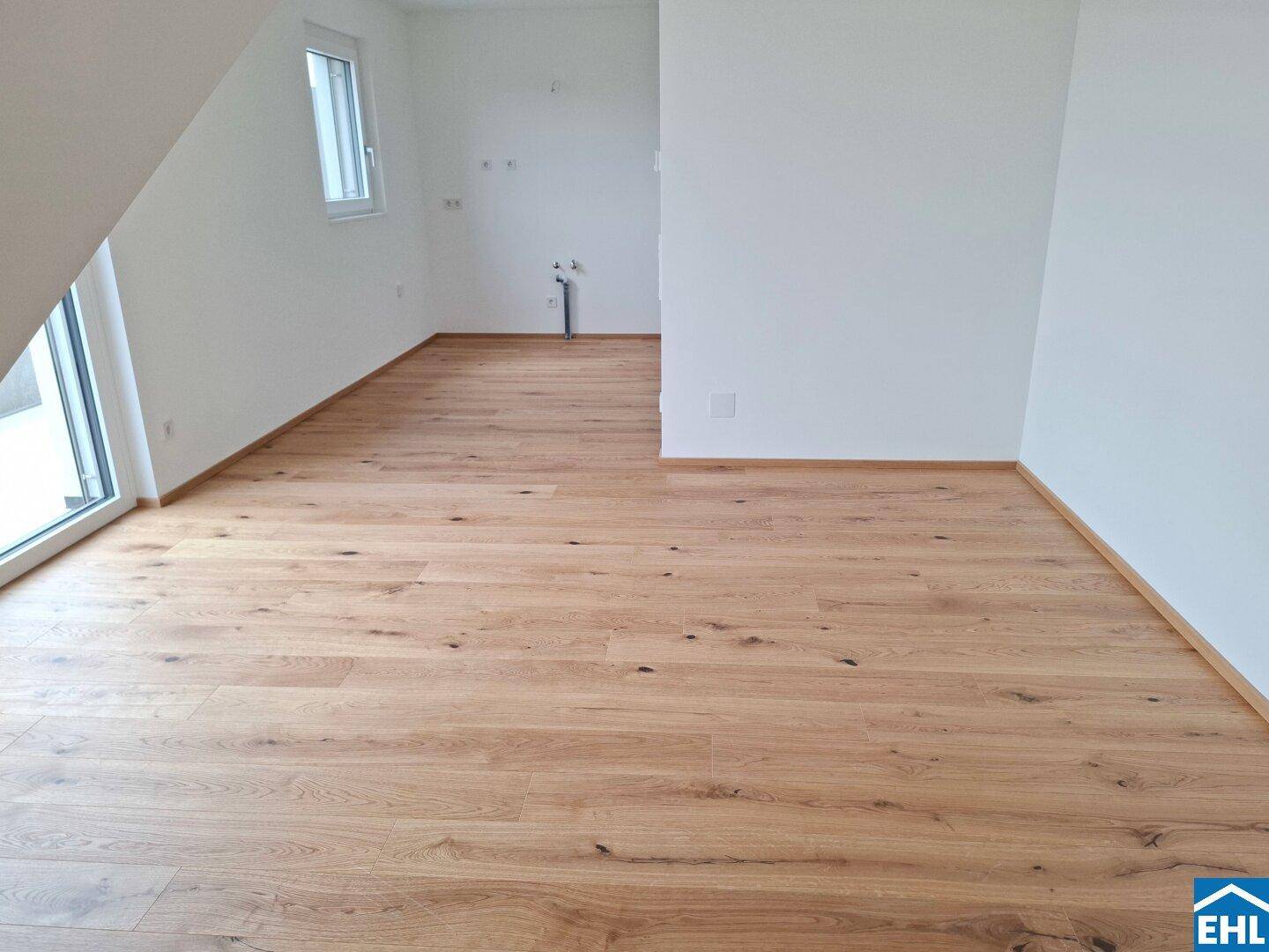 Geräumiger, unmöblierter Raum mit Holzboden, weißen Wänden und Zugang nach draußen.