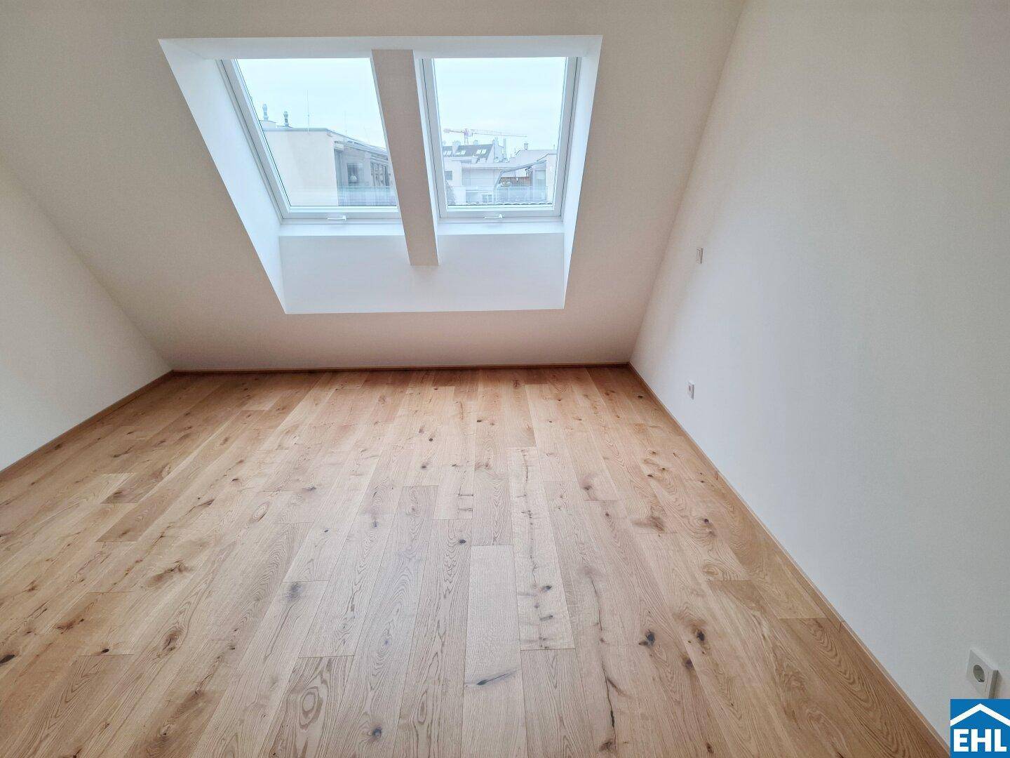 Geräumiges Dachzimmer mit zwei großen Dachfenstern und neuem Parkettboden, ideal für natürliches Licht.
