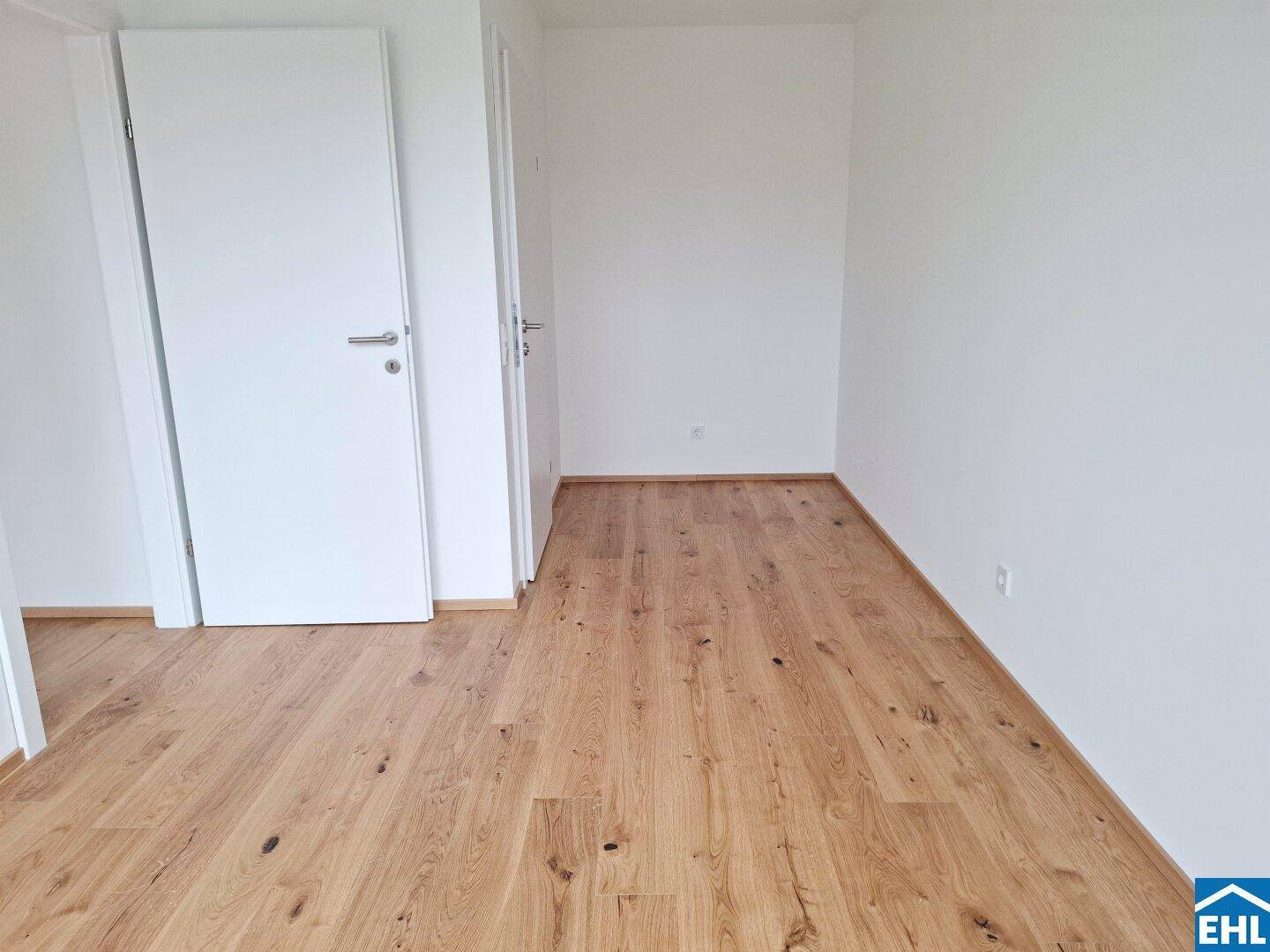 Leeres Zimmer mit hellem Holzboden und zwei weißen Türen, bereit zur individuellen Gestaltung.