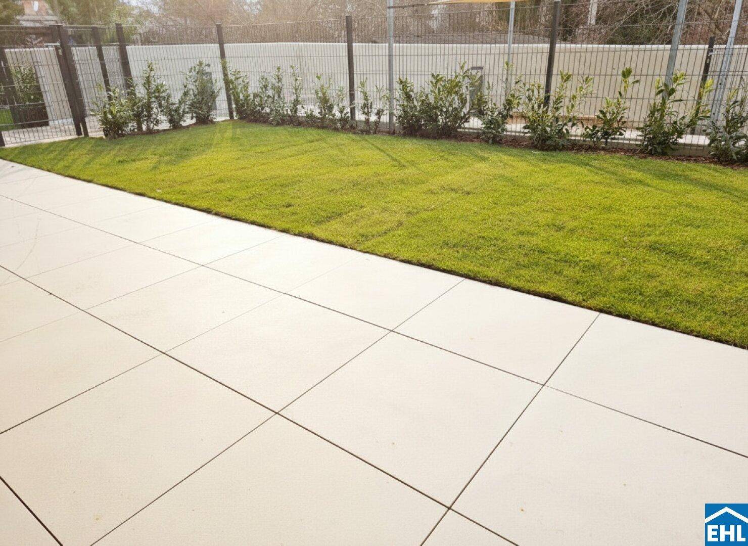 Gepflegte Terrasse mit großen hellen Fliesen und angrenzender Grünfläche.