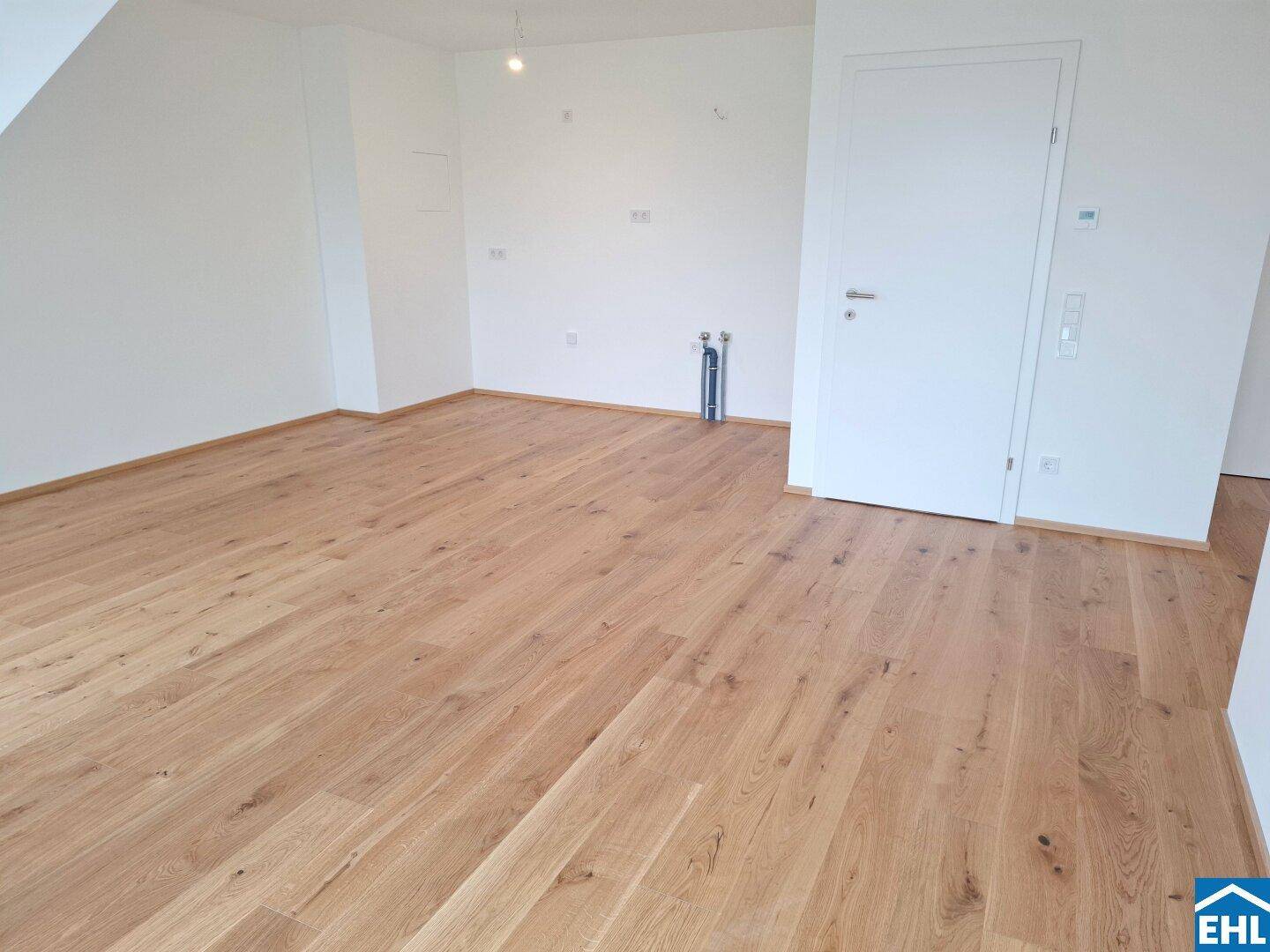 Leerer Raum mit Holzboden und Anschlüssen, ideal für eine Küche oder einen Hauswirtschaftsraum.