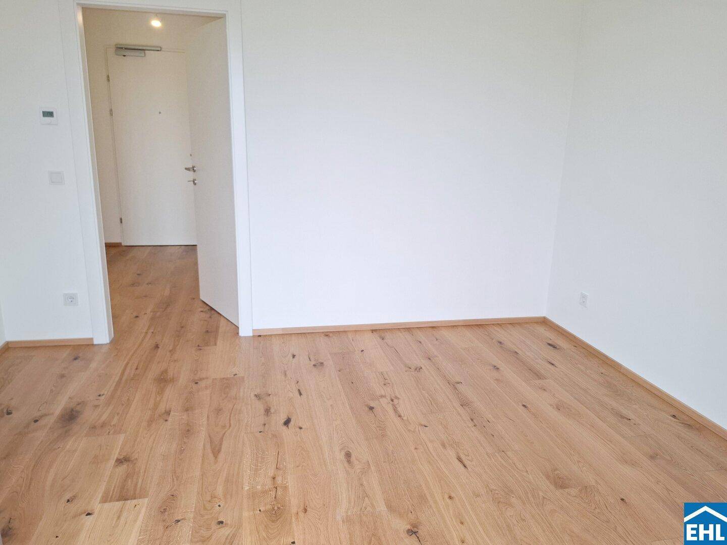 Leerer Raum mit hellem Holzboden und weiß gestrichenen Wänden.