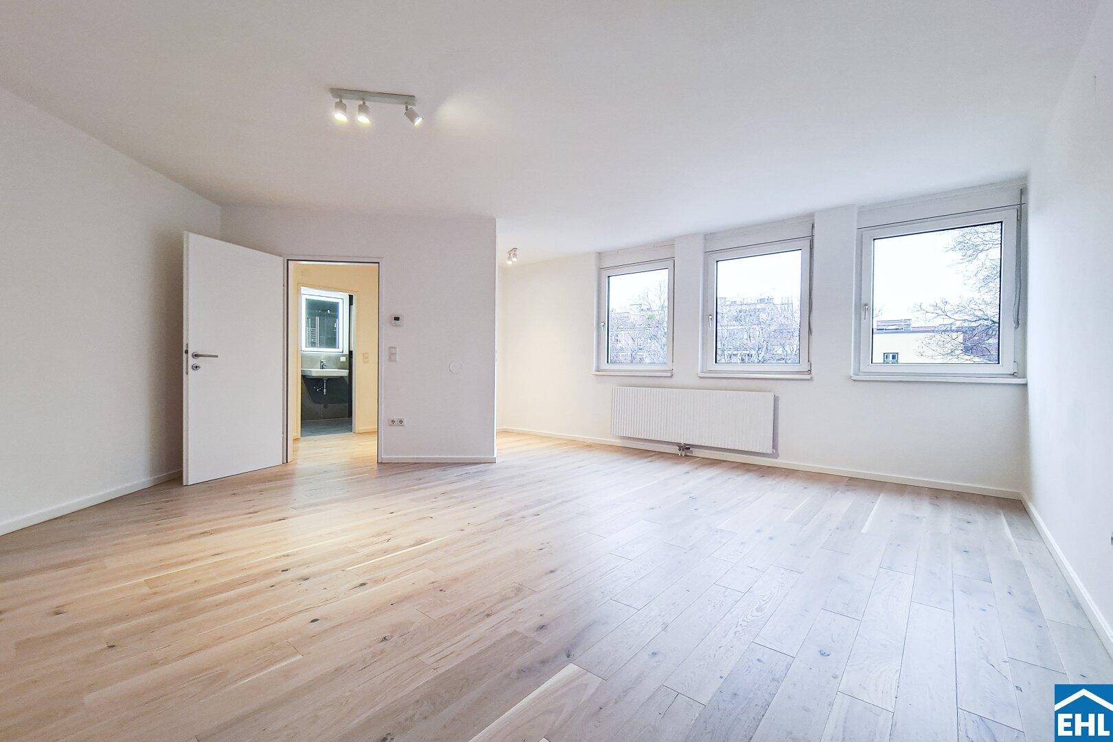 Heller Wohnraum mit Parkettboden und Blick durch die offene Tür in ein modernes Badezimmer.