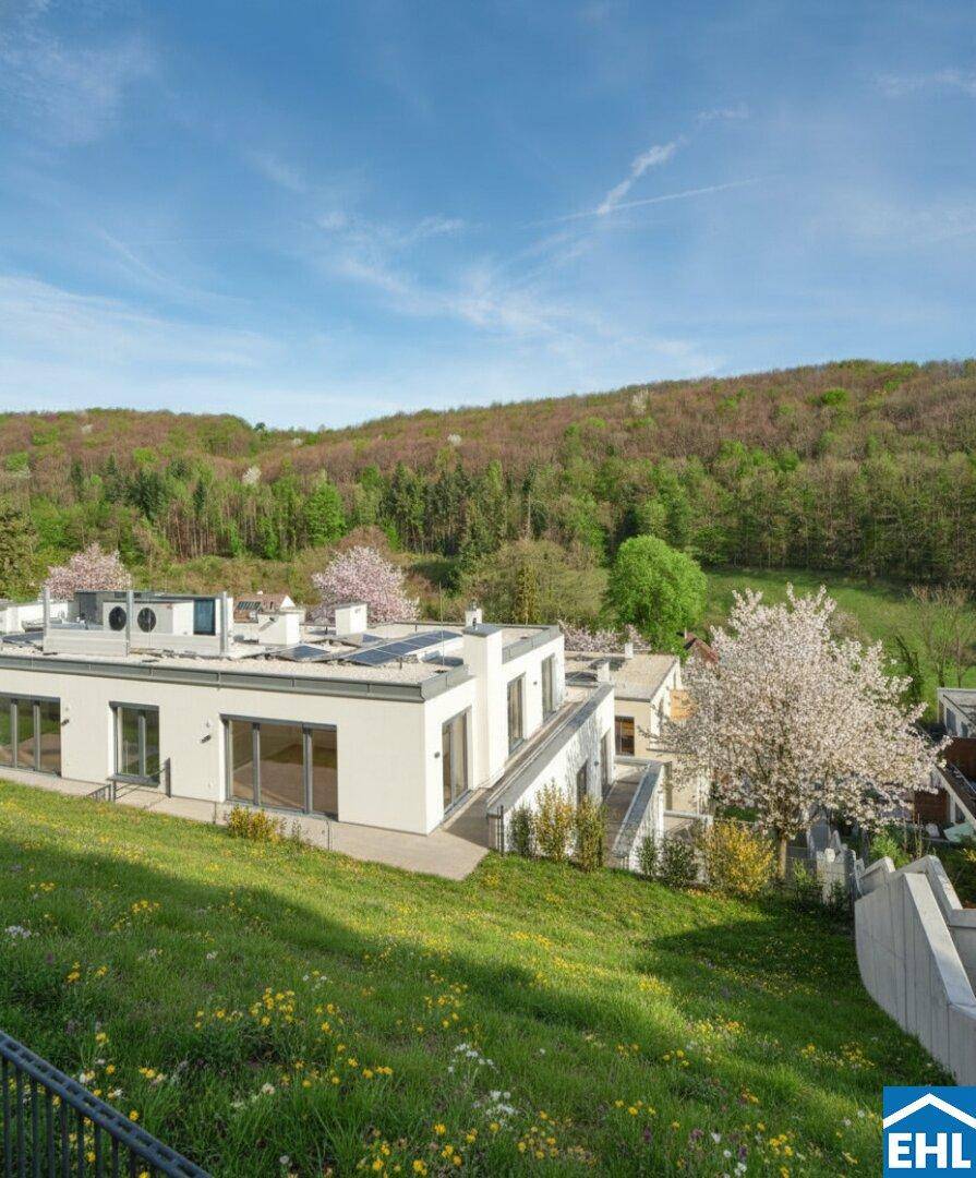 Moderne Gebäude in einer grünen Umgebung mit blühenden Bäumen und weitem Blick auf die Landschaft.