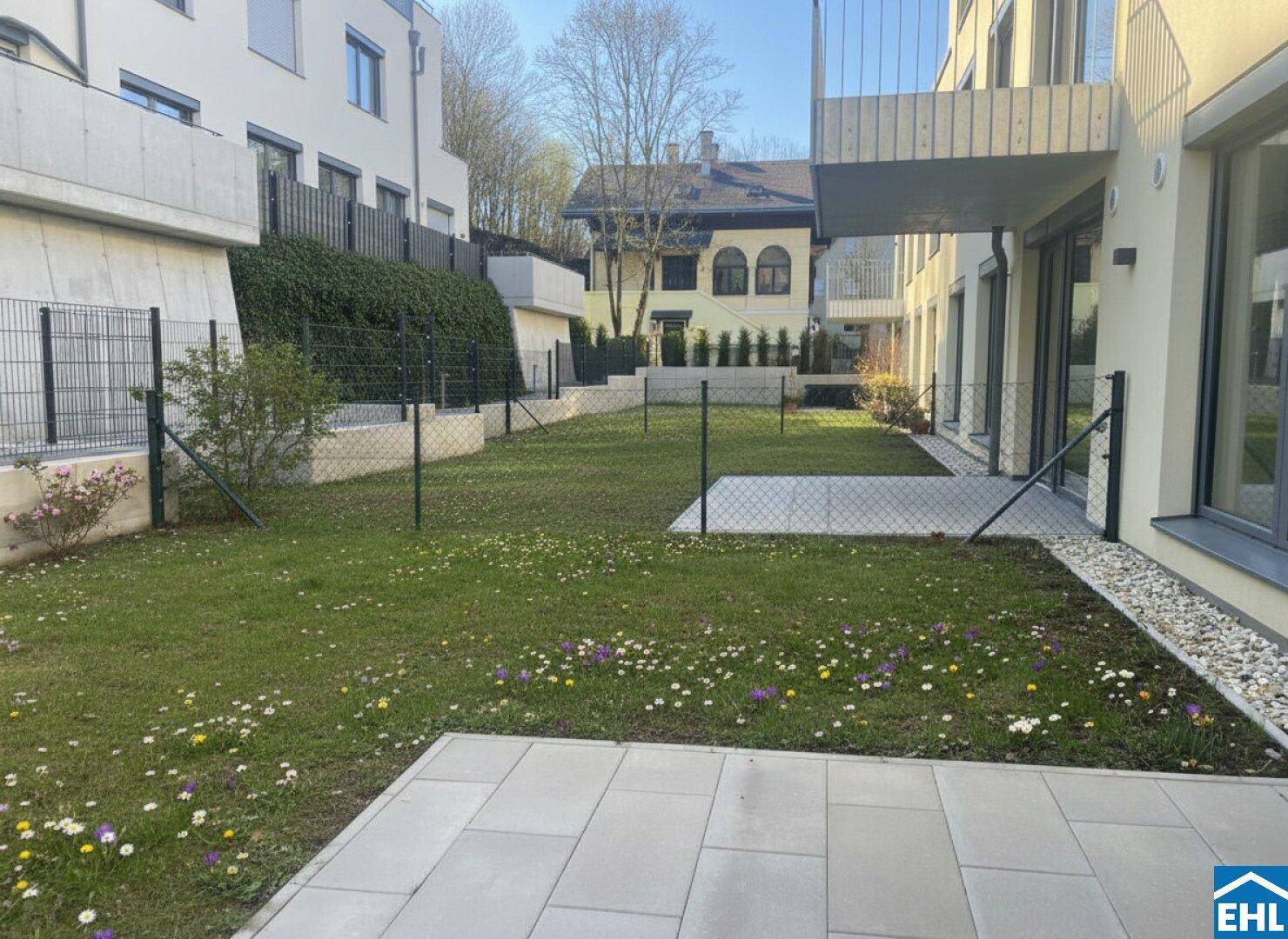 Gepflegter Gartenbereich mit Rasenfläche, bunten Blumen und einer gepflasterten Terrasse.