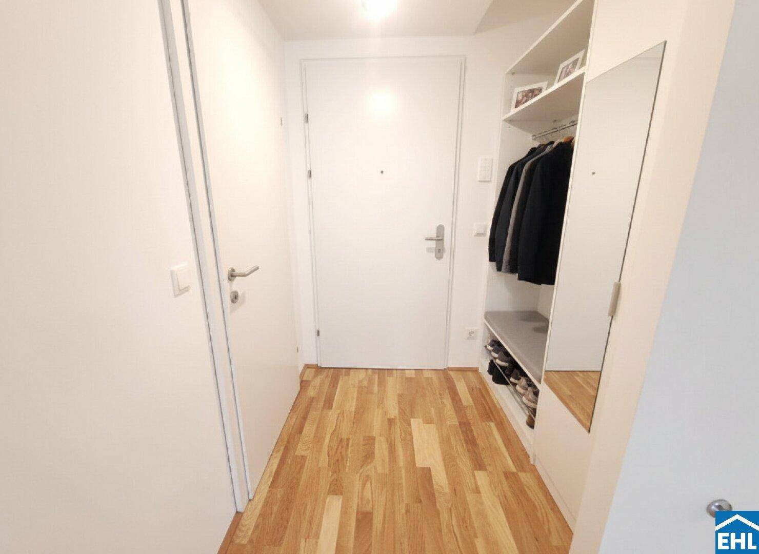 Heller Eingangsbereich mit Holzboden, integrierter Garderobe und einem großen Spiegel.