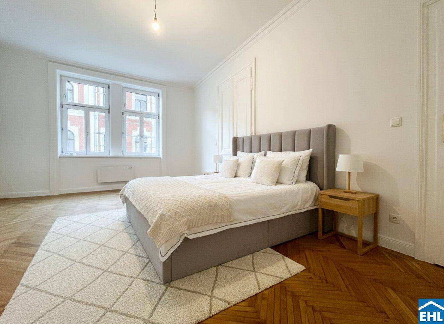 Geräumiges Schlafzimmer mit großem Bett, Fischgrätparkett und zwei hohen Fenstern.