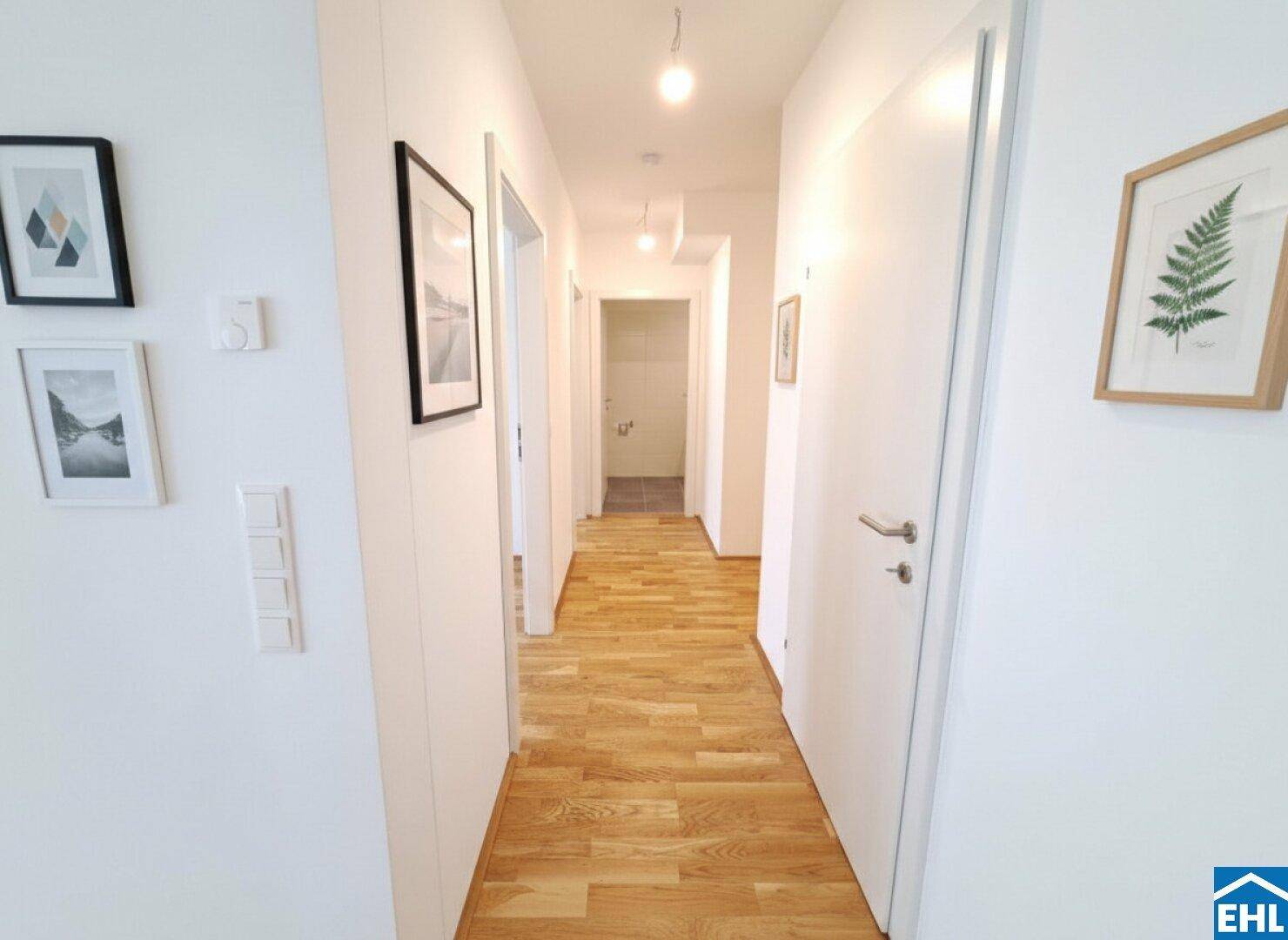 Heller Flur mit Parkettboden und weißen Wänden, führt zu den verschiedenen Räumen der Wohnung.