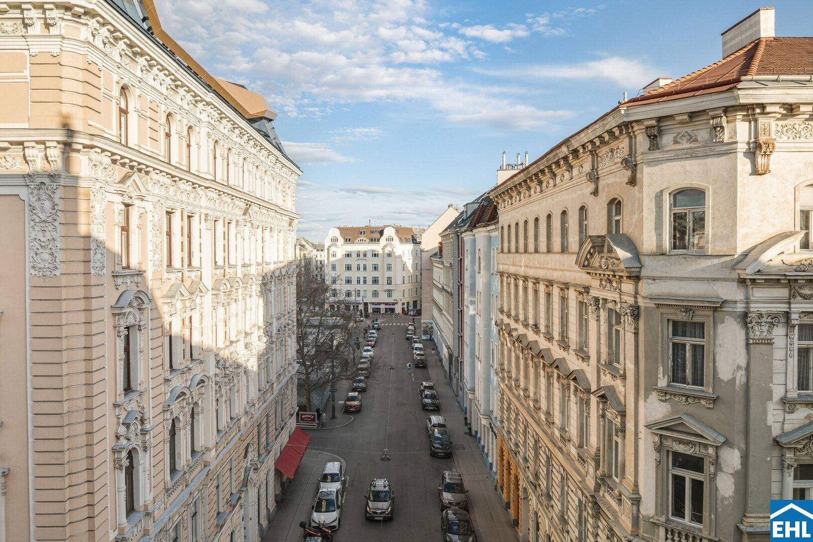 Blick von oben auf eine belebte Straße mit historischen Gebäuden und parkenden Autos.