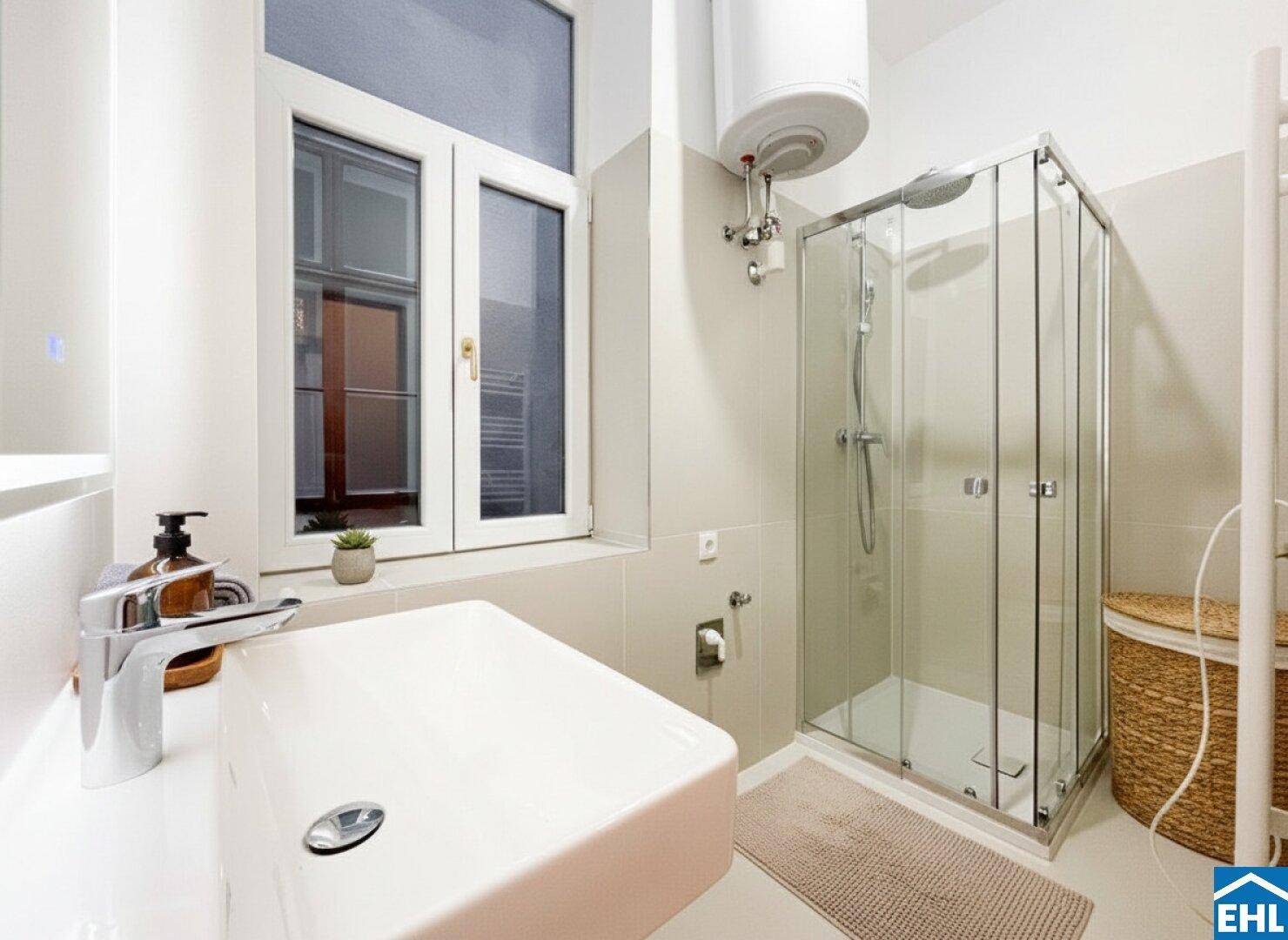 Funktionales Badezimmer mit Waschbecken, Duschkabine und Fenster für Tageslicht.