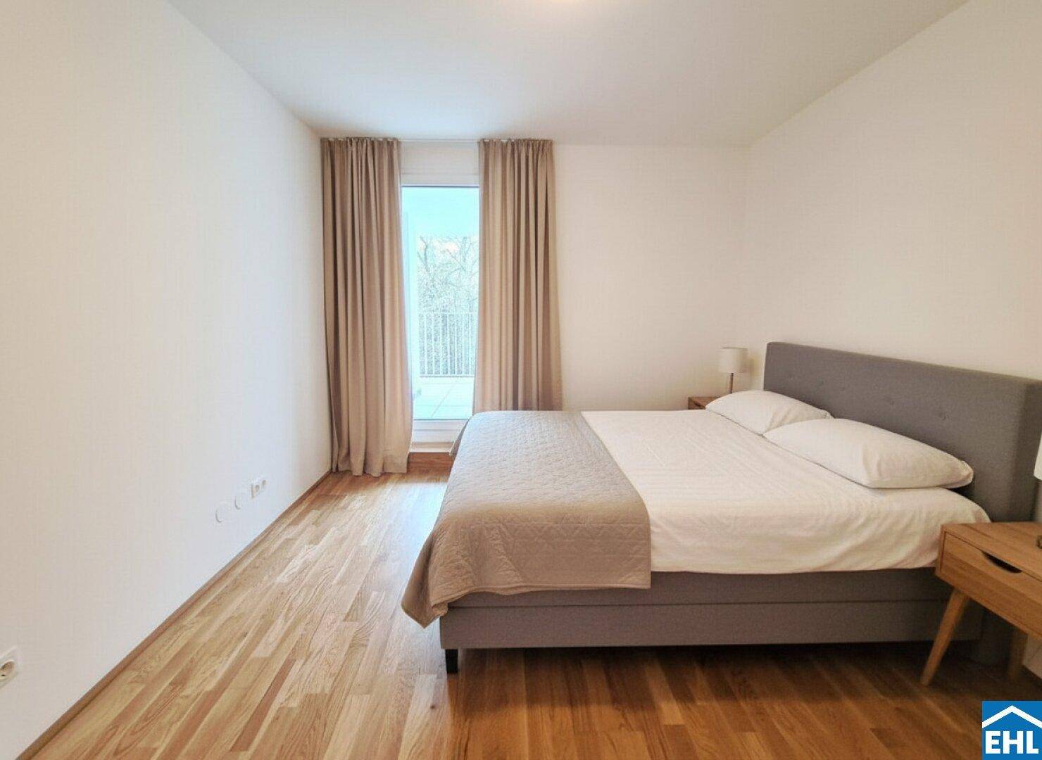 Helles Schlafzimmer mit Holzboden, Doppelbett und direktem Zugang zu einem Balkon.