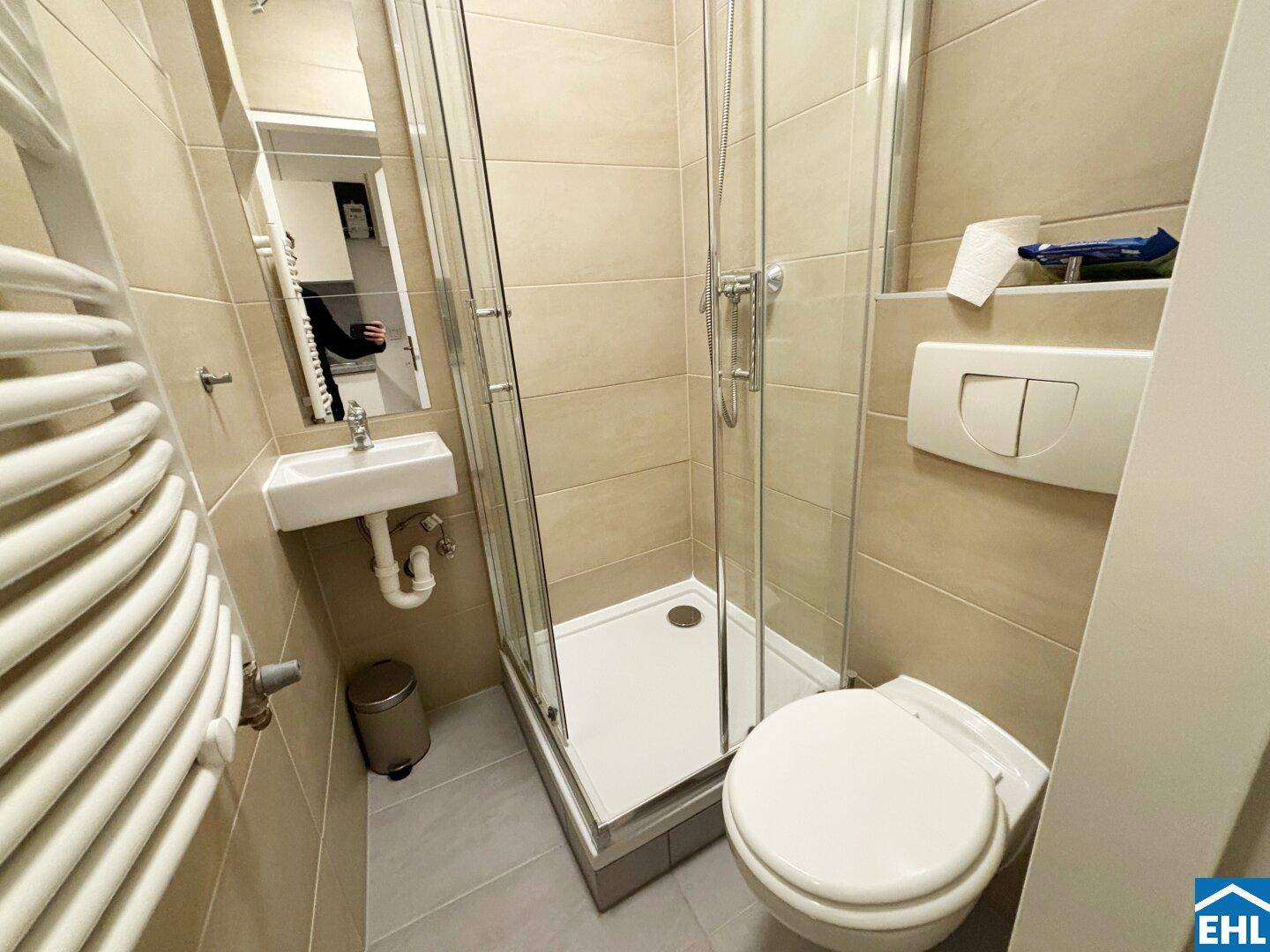 Modernes Badezimmer mit Duschkabine, WC, kleinem Waschbecken und Handtuchheizkörper.