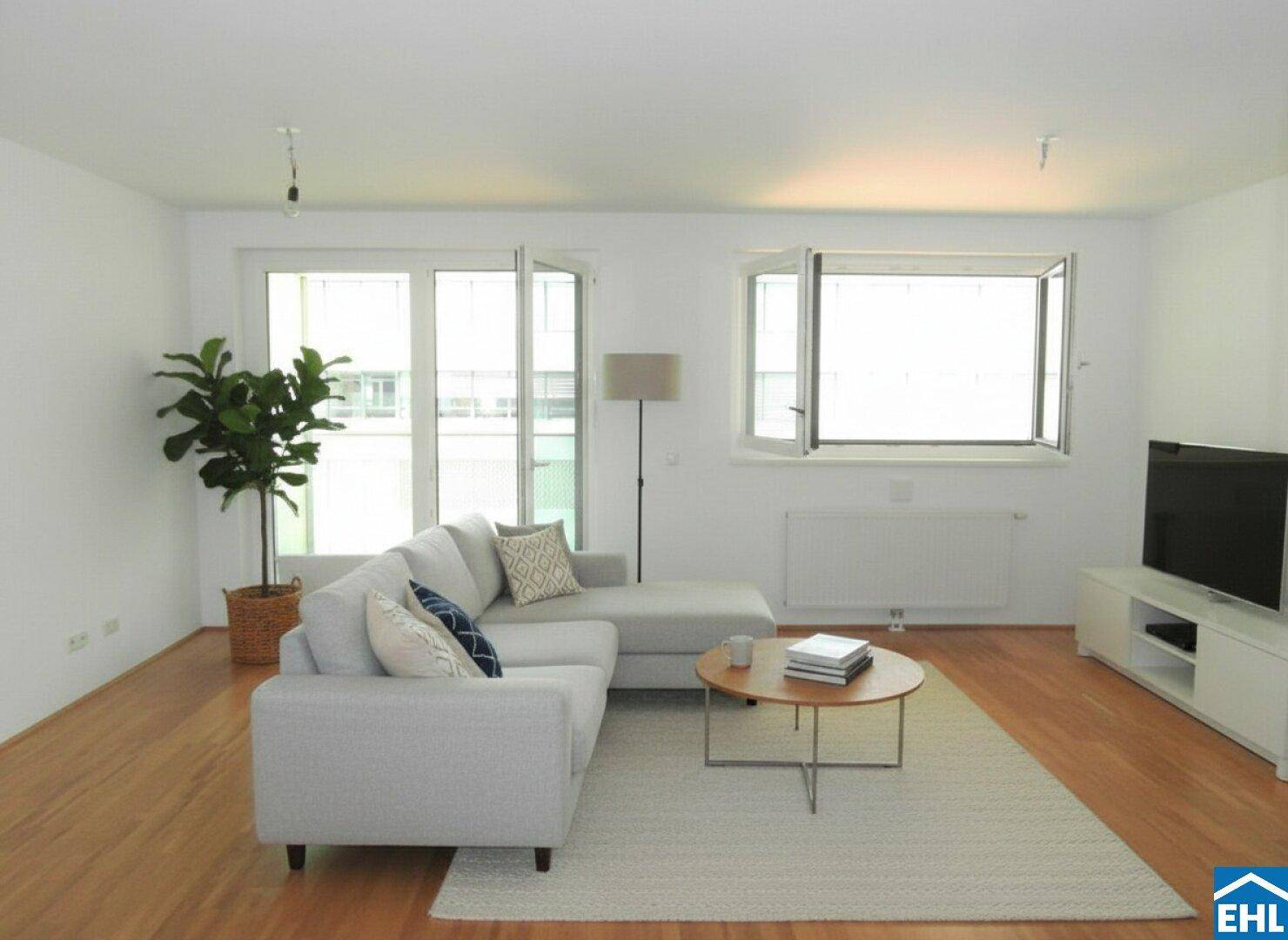 Lichtdurchflutetes Wohnzimmer mit großen Fenstern und modernem Sofa.