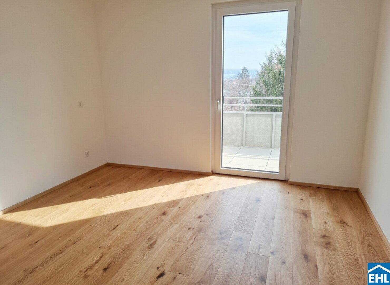 Lichtdurchfluteter Raum mit Holzboden und direktem Zugang zu einem sonnigen Balkon.