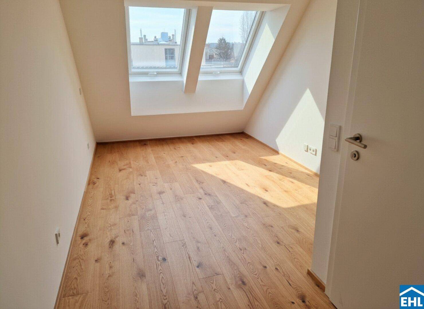 Helles Schlafzimmer im Dachgeschoss mit Holzboden, schrägen Wänden und Dachfenstern.