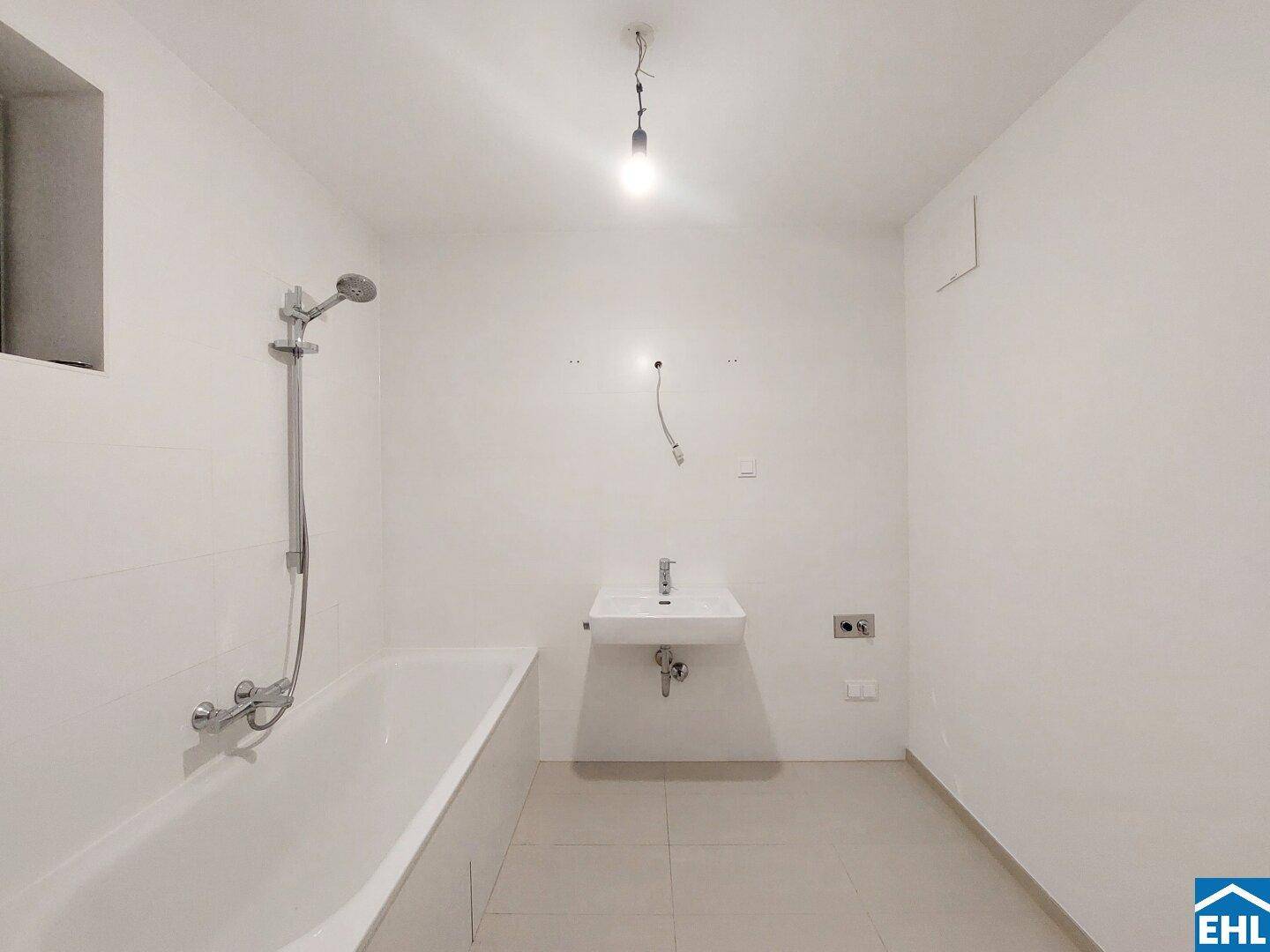 Modernes Badezimmer mit Badewanne, wandmontiertem Waschbecken und hellen Fliesen an Wänden und Boden.