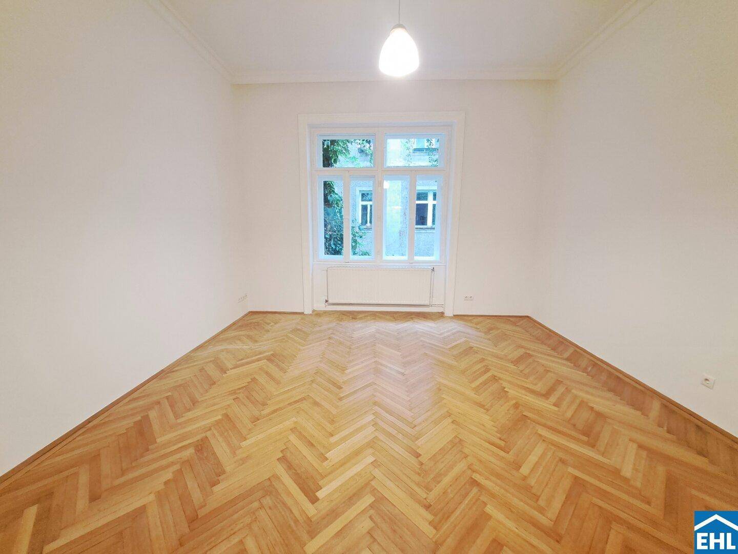 Heller Raum mit klassischem Fischgrätparkett und großem Fenster für viel Tageslicht.