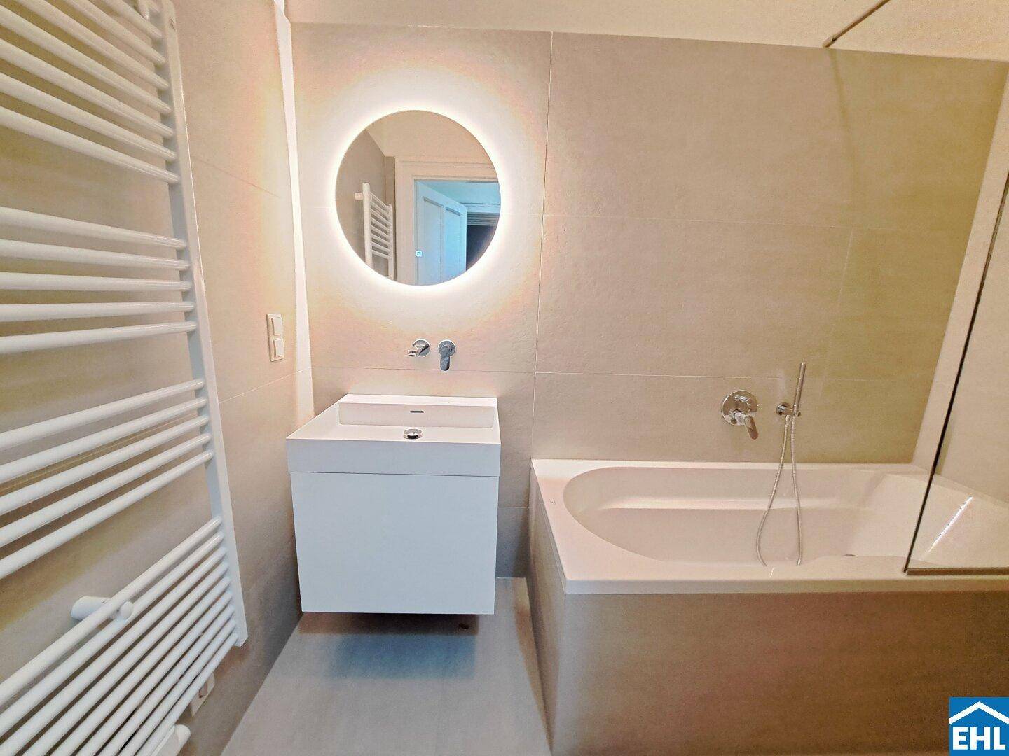 Modernes Badezimmer mit beleuchtetem Spiegel, Waschtisch und Badewanne.
