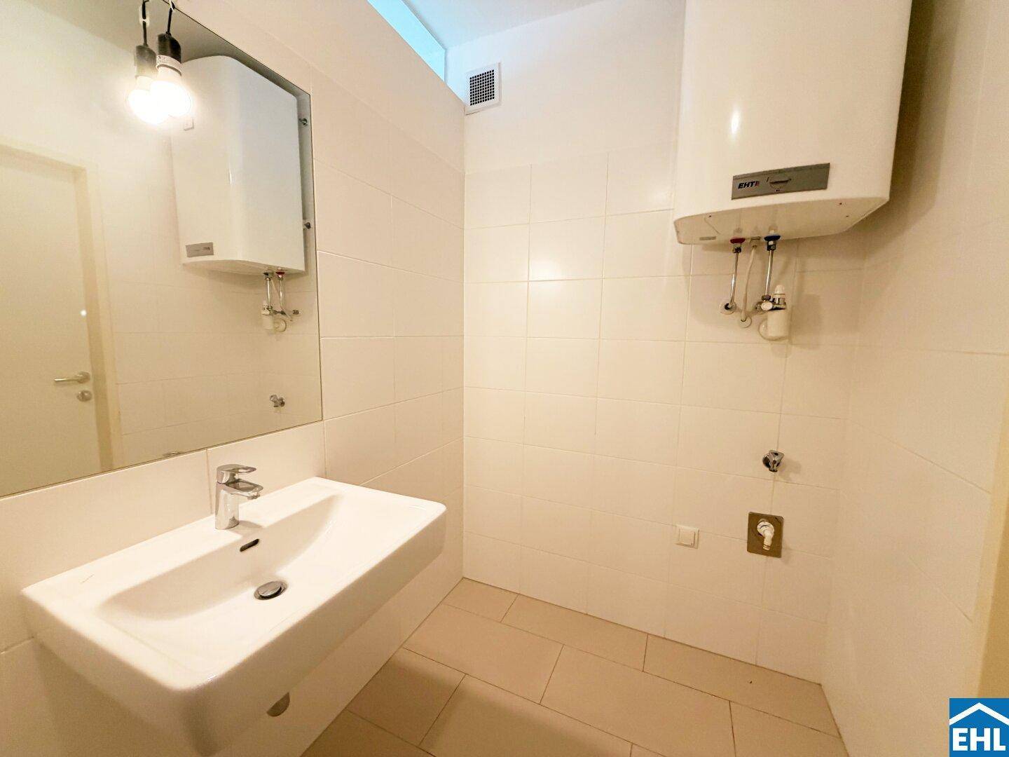 Funktionales Badezimmer mit Waschbecken, Spiegel und Warmwasserboiler an der Wand.