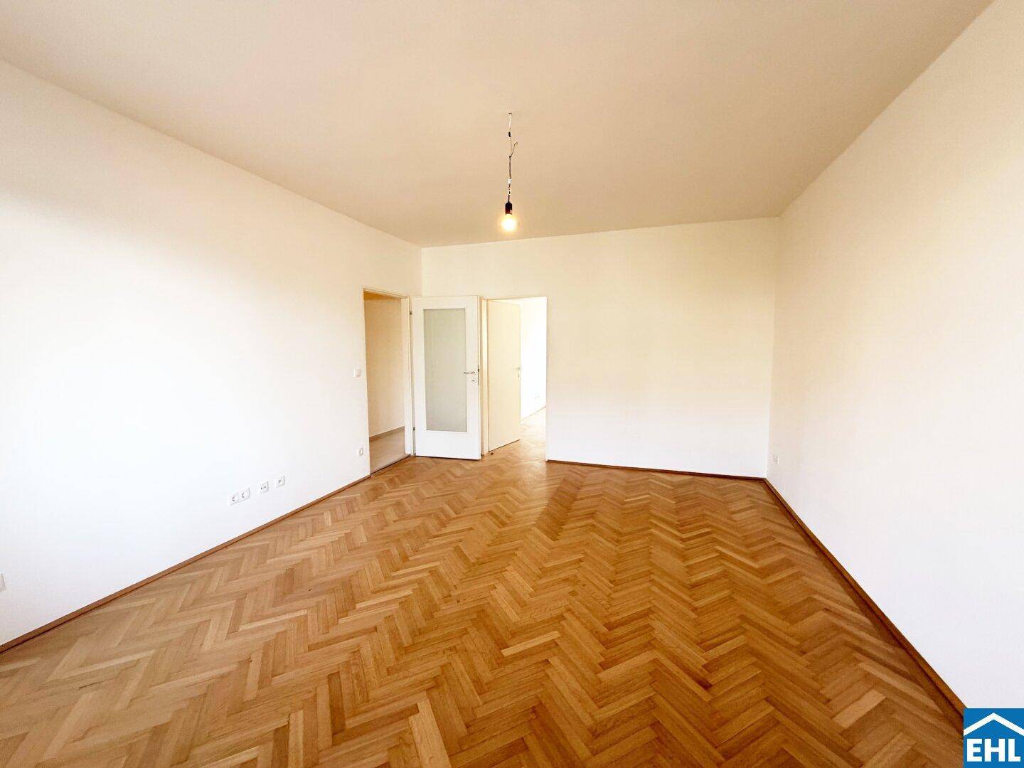 Geräumiges Wohnzimmer mit klassischem Fischgrätparkett und Türen zu weiteren Räumen.