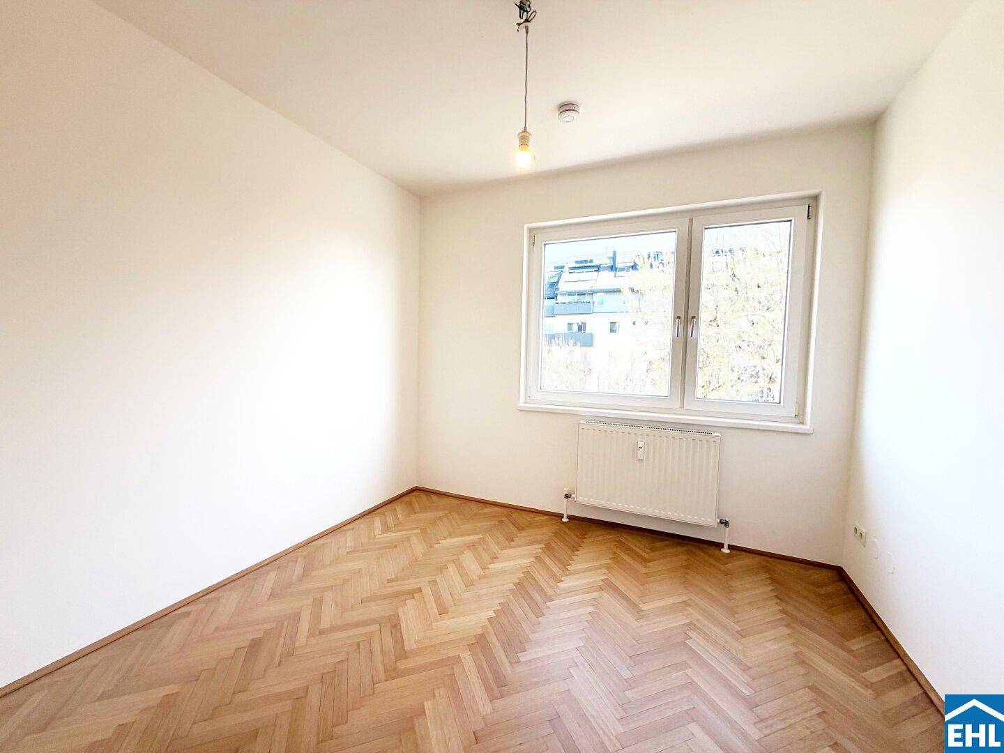 Helles Schlafzimmer mit Fischgrätparkett und einem großen Fenster für viel Tageslicht.
