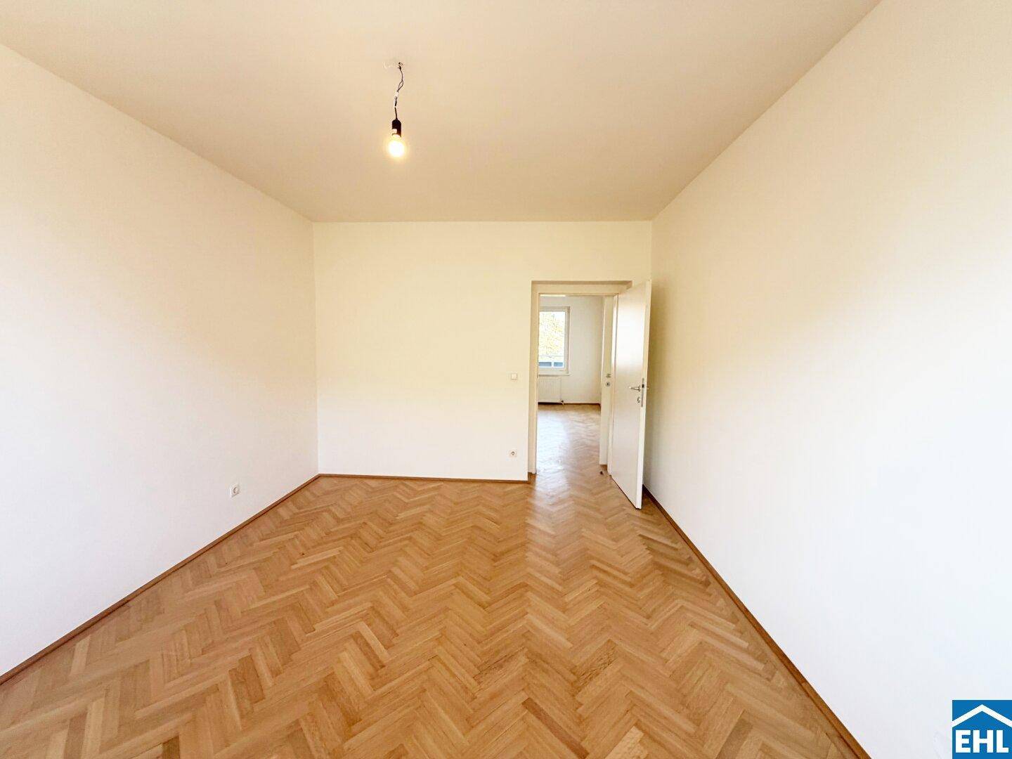Freundliches Schlafzimmer mit Fischgrätparkett und weiß gestrichenen Wänden, bereit zum Einrichten.