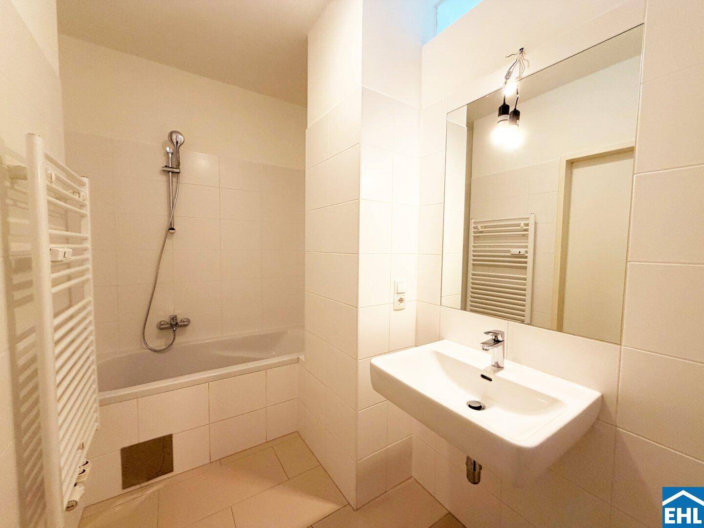 Modern gefliestes Badezimmer mit Badewanne, Waschbecken und beheiztem Handtuchhalter.