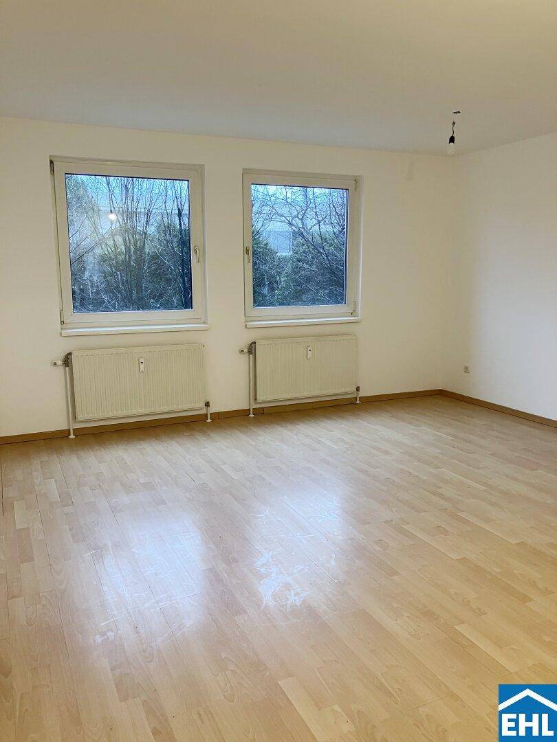 Geräumiges Zimmer mit hellem Parkettboden und Blick ins Grüne durch zwei Fenster, in gepflegtem Zustand.