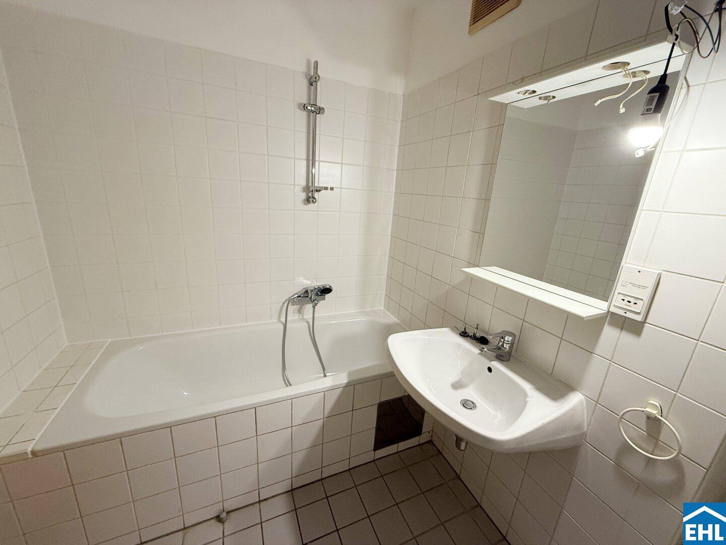 Badezimmer mit Badewanne, Waschbecken und weißen Fliesen an Wänden und Boden.
