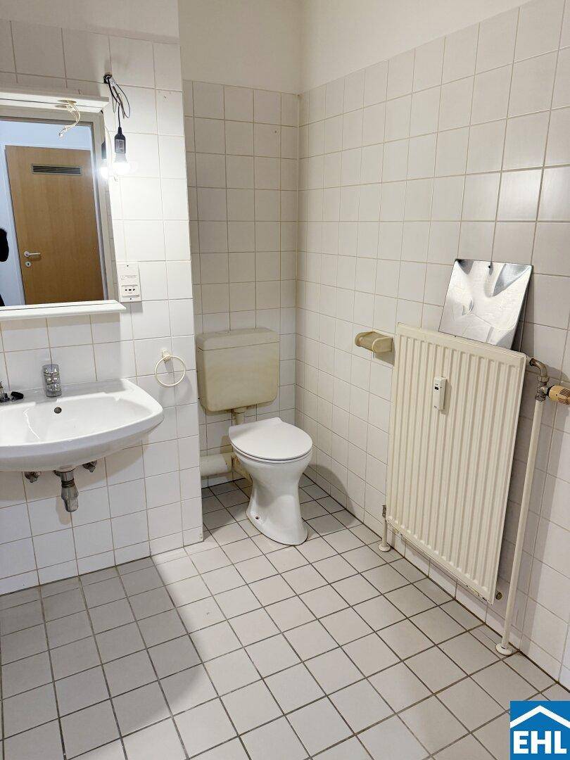 Separates WC mit Toilette, Waschbecken und weißen Wand- und Bodenfliesen.