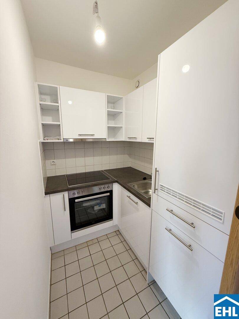 Kleine, moderne Küche mit weißen Hochglanzschränken, Einbaugeräten und Fliesenboden.