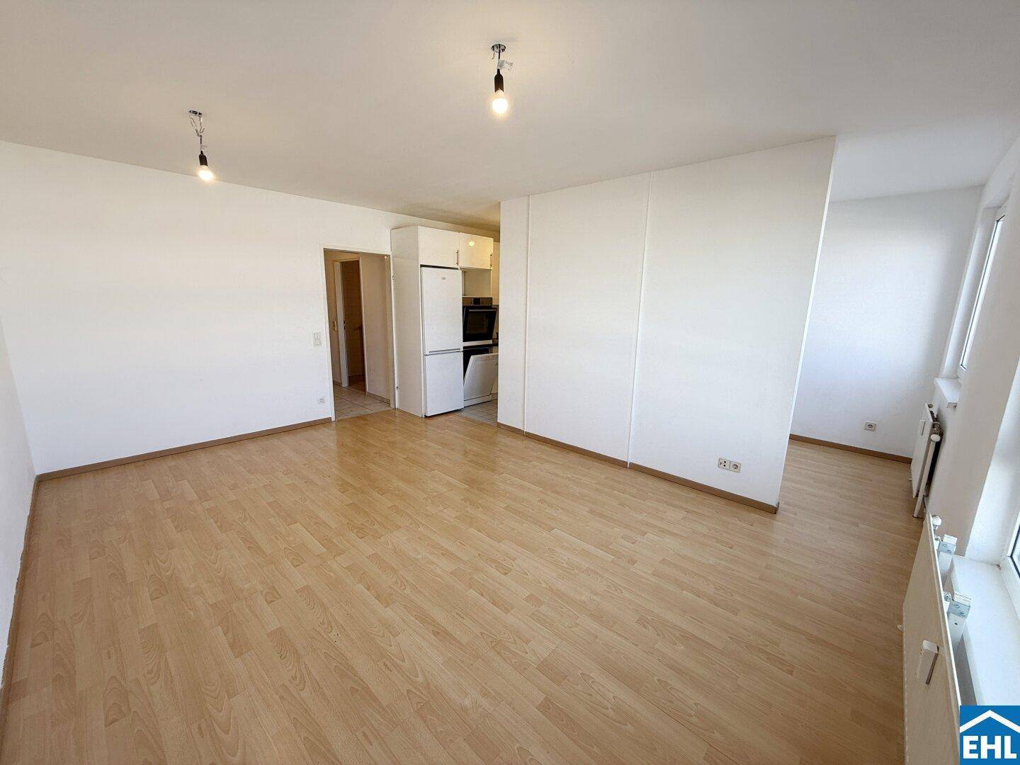 Geräumiger Wohnbereich mit Holzfußboden und Blick auf eine integrierte Küchenzeile.