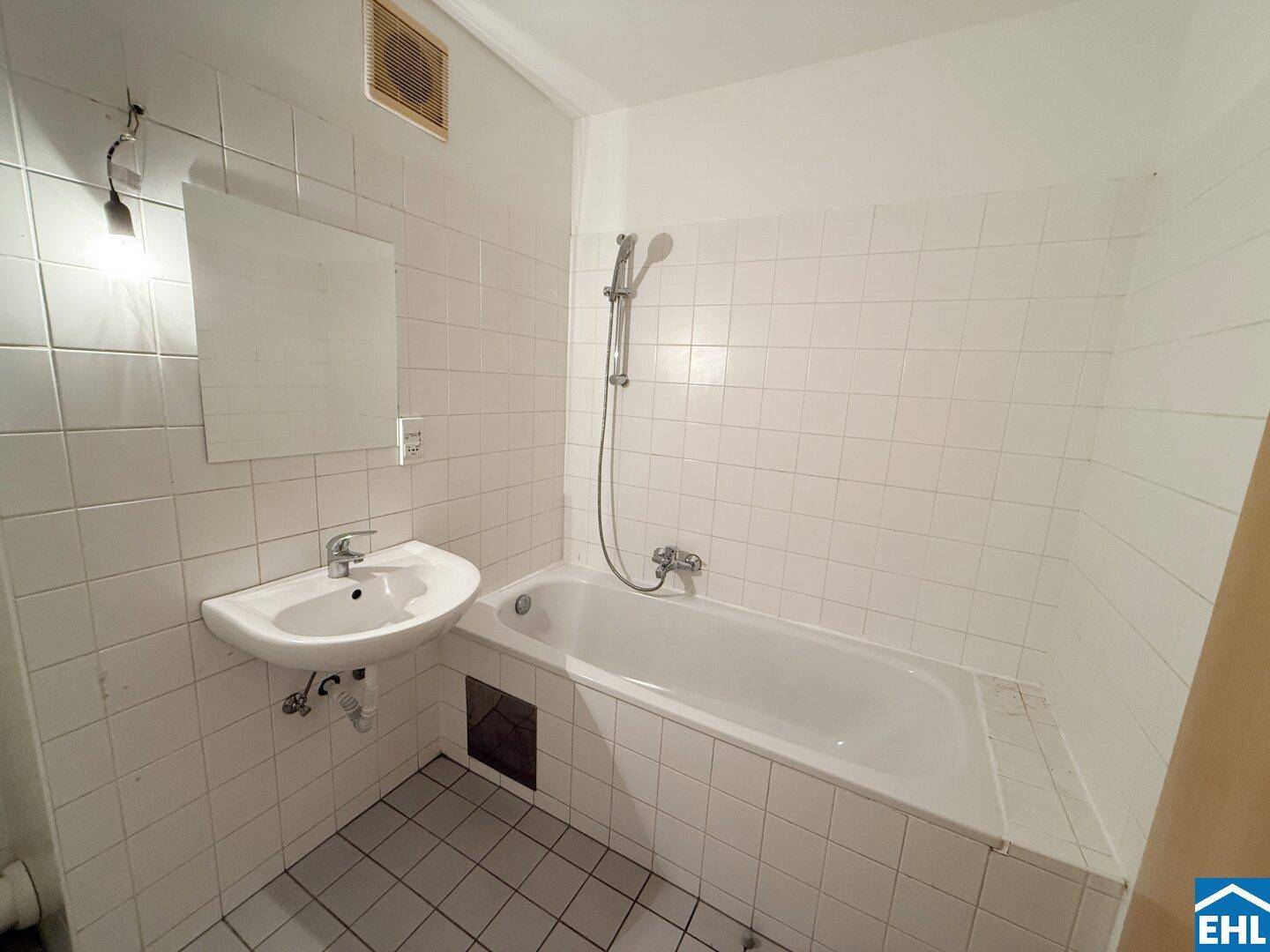Gefliestes Badezimmer mit Badewanne, Waschbecken und weißer Wandverkleidung.