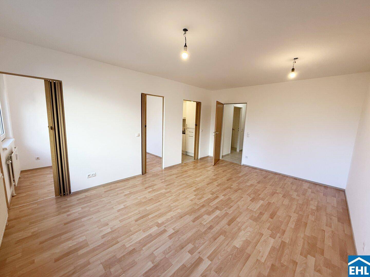 Geräumiges, helles Zimmer mit Laminatboden und mehreren Türen zu angrenzenden Räumen.