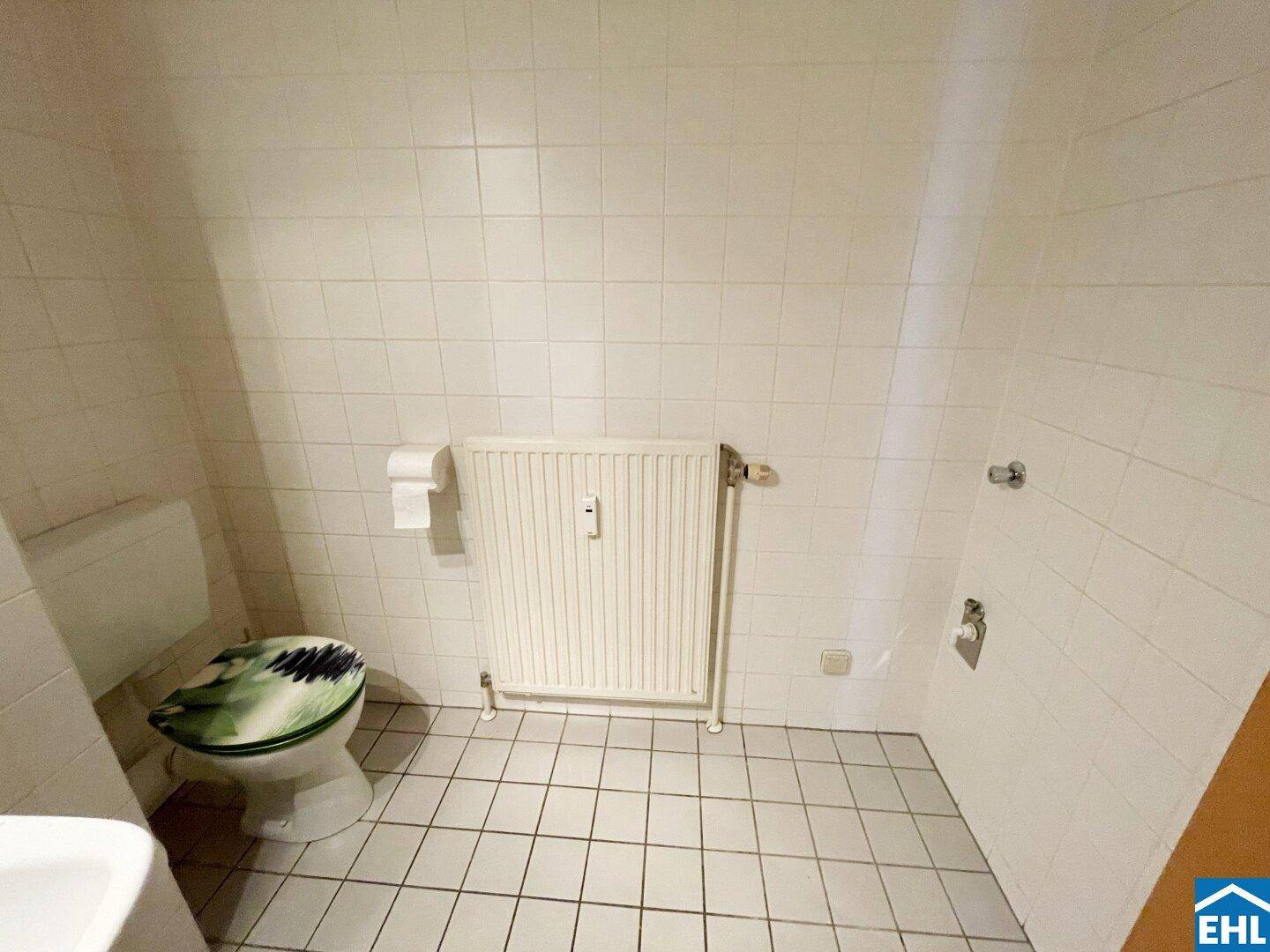 Separates WC mit Toilette und Heizkörper, komplett gefliest in Weiß.