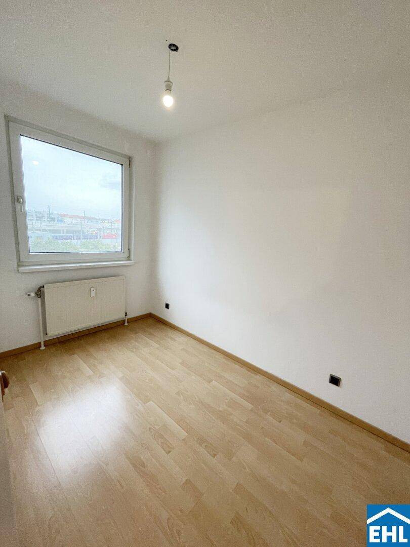 Helles Schlafzimmer mit Parkettboden und großem Fenster, bietet viel Tageslicht.