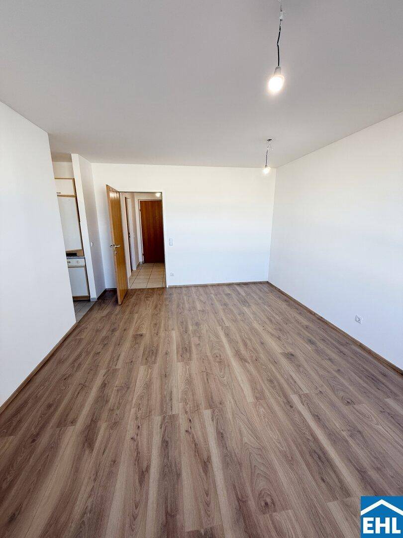 Leerer Wohnbereich mit Laminatboden und weiß gestrichenen Wänden, bietet viel Gestaltungsfreiheit.