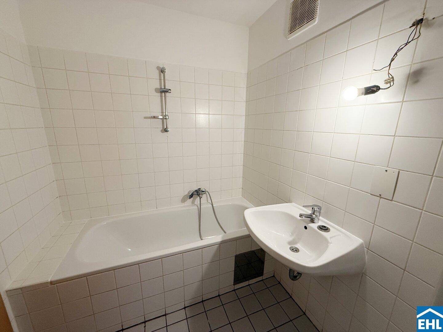 Badezimmer mit Badewanne, weiß gefliesten Wänden und einem Waschbecken.