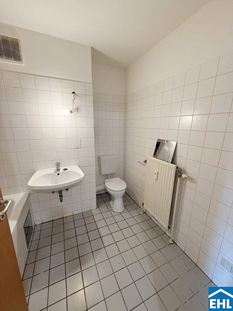 Badezimmer mit WC, Waschbecken und Heizkörper, komplett weiß gefliest.